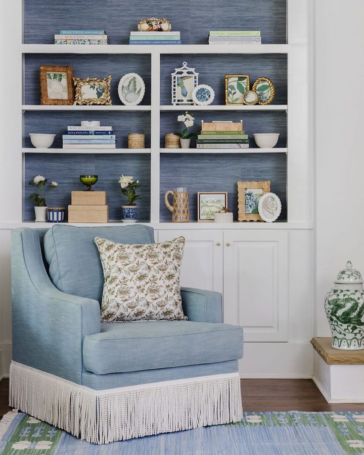 A blue and white living room with society social classic faux grasscloth peel and stick nuwallpaper on the bookshelves and a matching textured chair.