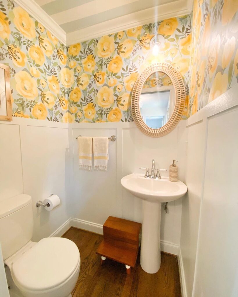 Yellow and blue peel and stick NuWallpaper makes this powder room feel bright and spacious with white board and batten paneling along the walls and rattan mirror frame
